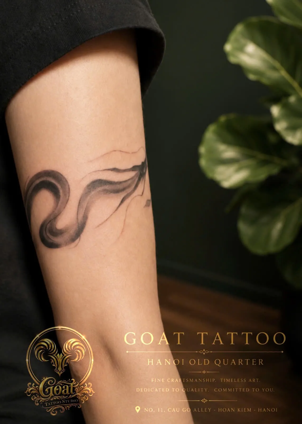 A flowing black ink-wash swirl tattoo with soft brushstroke texture wrapping the forearm, done at GOAT Tattoo Studio in Hanoi's Old Quarter.