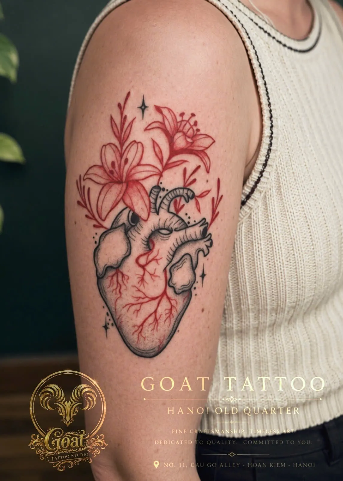Illustrative anatomical heart tattoo with red lily flowers on the upper arm, by GOAT Tattoo Studio Hanoi.