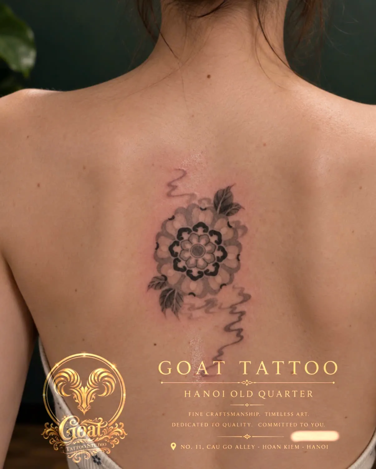 A black and grey peony flower with flowing smoke-like ribbons, tattooed on the upper back, by GOAT Tattoo Studio Hanoi.