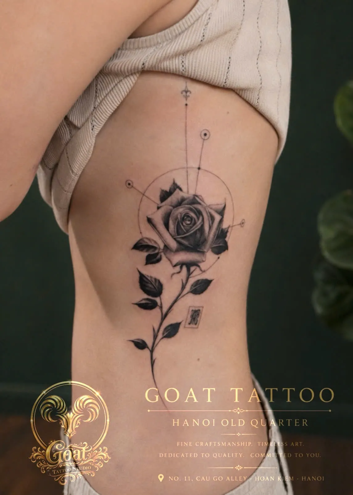 A black and grey realism rose tattoo framed by fine line sacred geometry, down the ribs, by GOAT Tattoo Studio Hanoi.