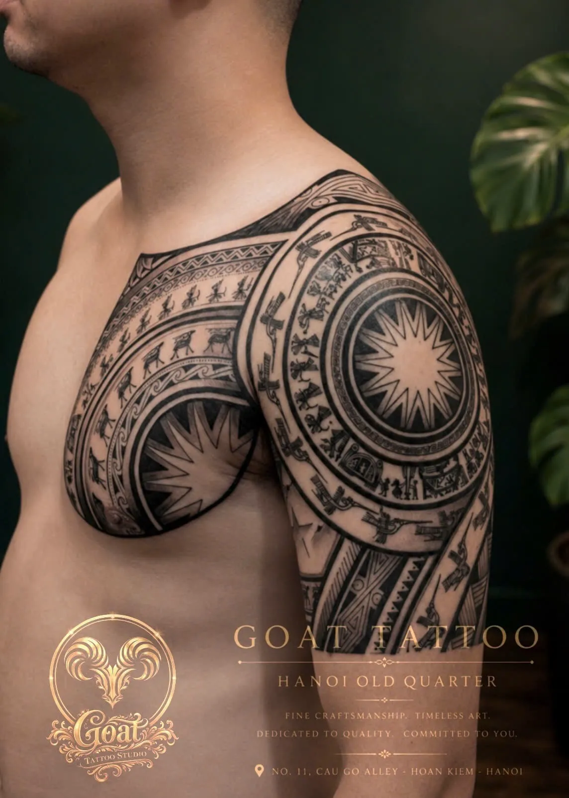 Blackwork tribal tattoo with a sunburst medallion and animal motifs across the chest and shoulder, by GOAT Tattoo Studio Hanoi.