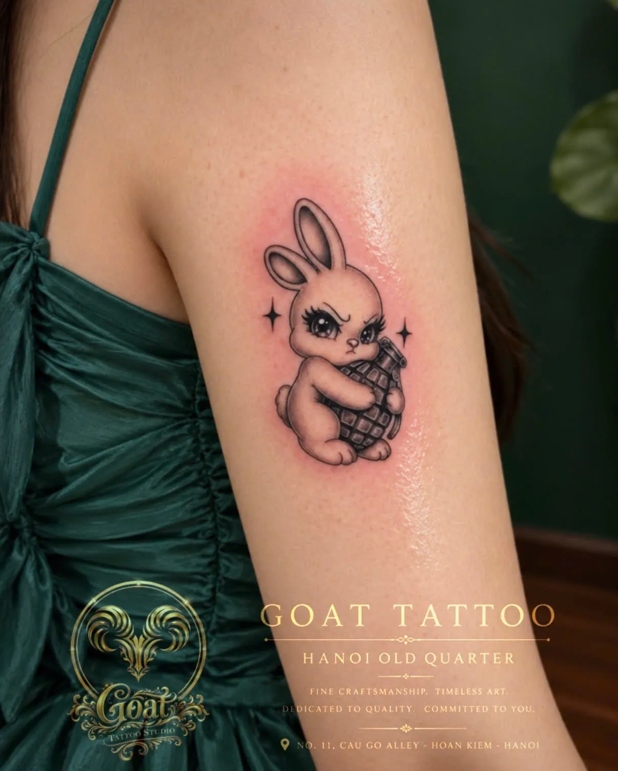 A black and grey illustrative tattoo of a cute bunny hugging a grenade, on the upper arm, by GOAT Tattoo Studio Hanoi.