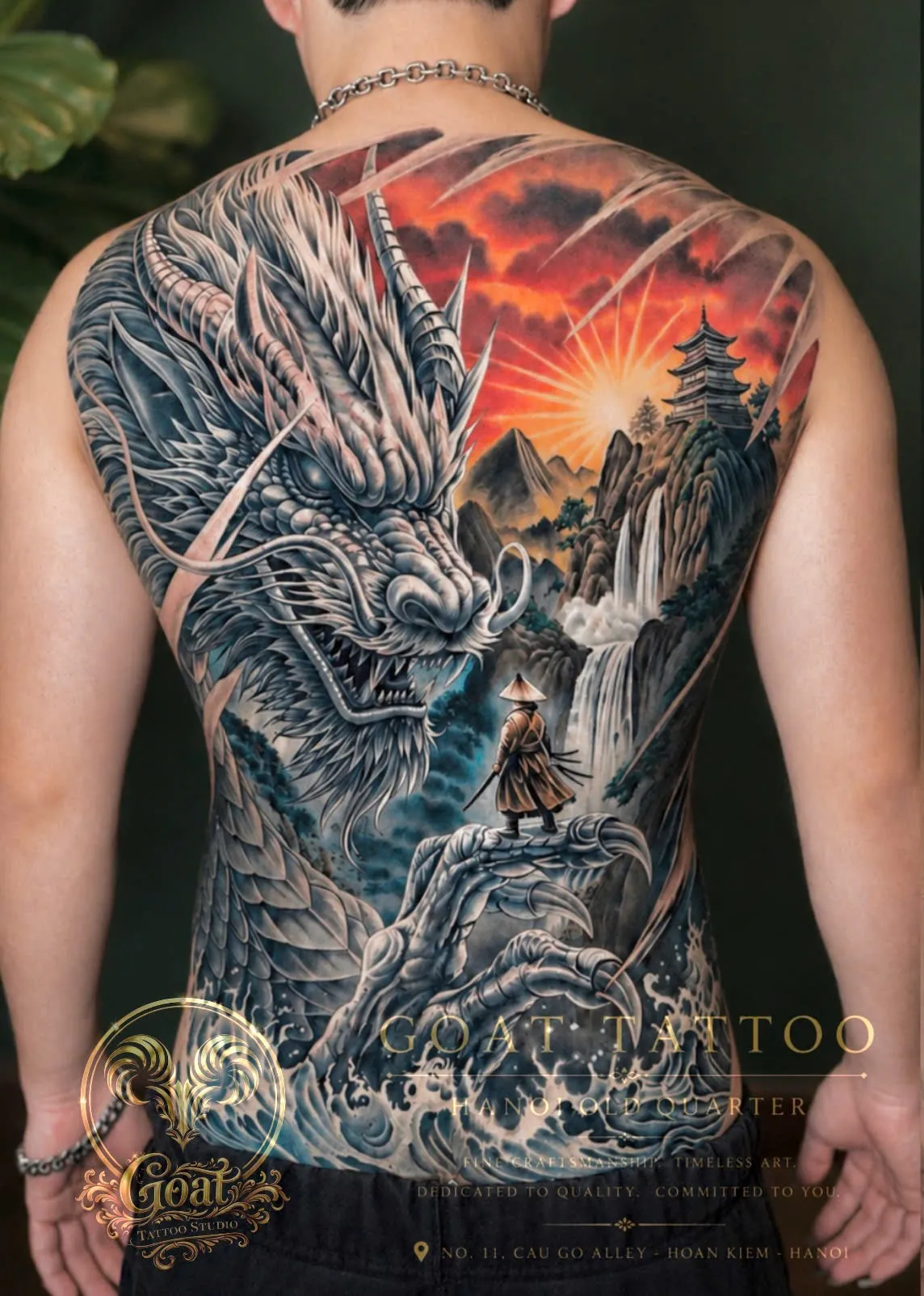 A vivid full back tattoo of a great horned dragon watching over a robed traveler standing before a waterfall and mountain pagoda at sunset, done at GOAT Tattoo Studio in Hanoi's Old Quarter.