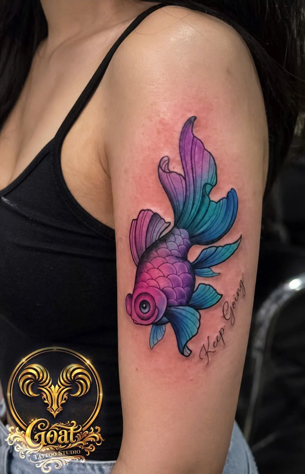 Purple and teal gradient goldfish tattoo with 'Keep Going' script on the upper arm, GOAT Tattoo Studio Hanoi.