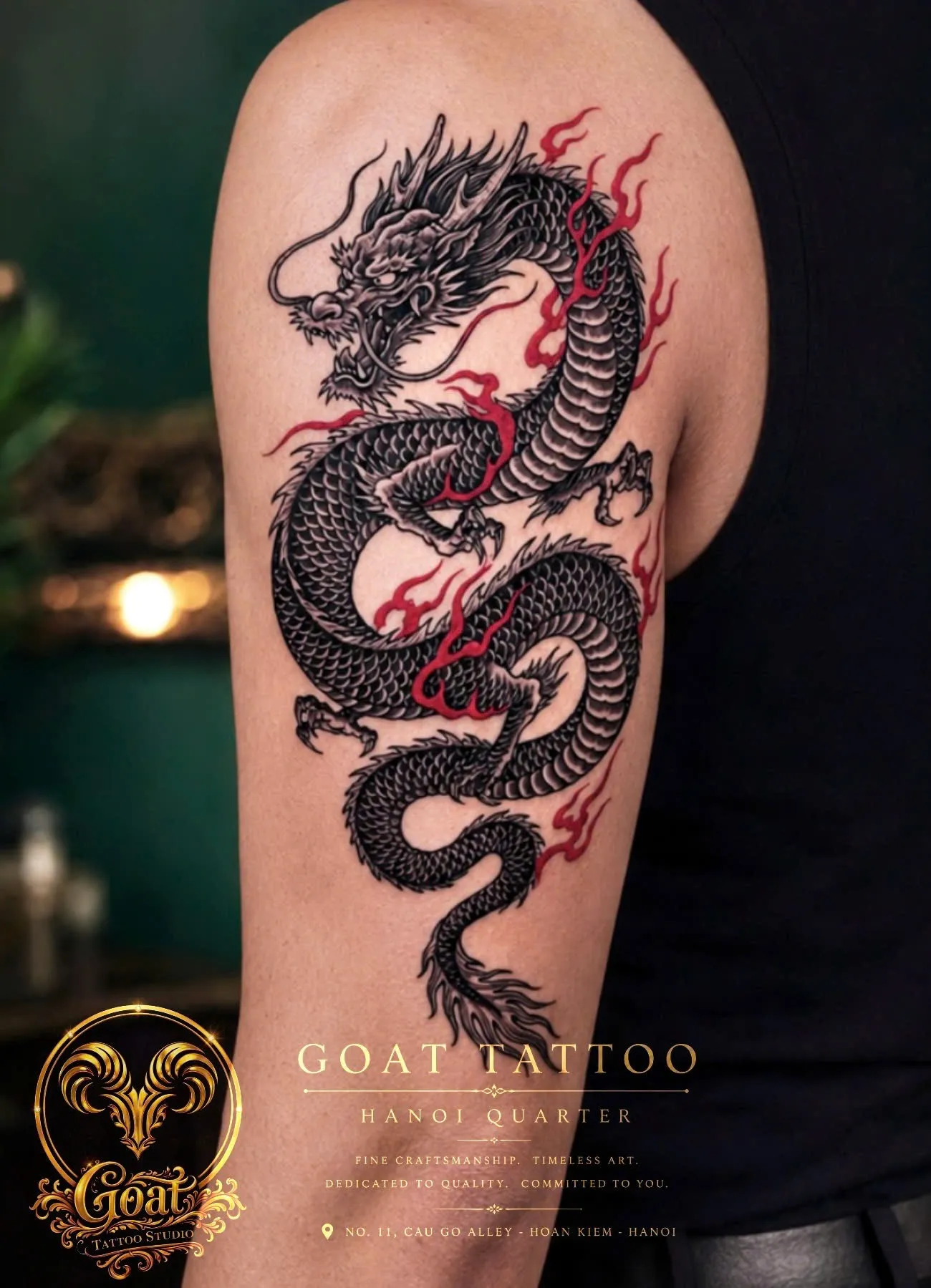 Black Japanese-style dragon tattoo with red flame accents covering the upper arm, by GOAT Tattoo Studio, Hanoi.