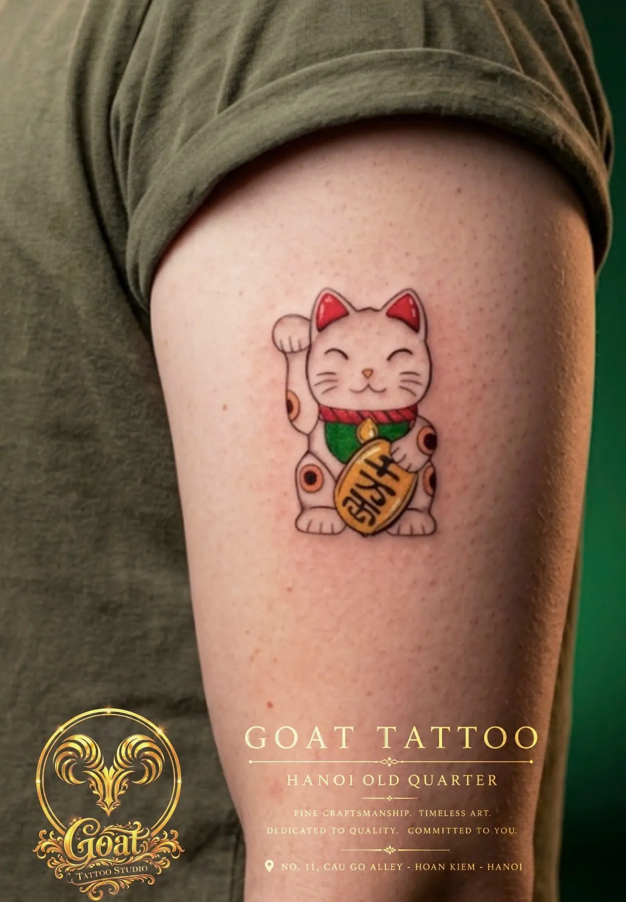 Color Japanese-style maneki-neko lucky cat tattoo with gold coin on the upper arm, by GOAT Tattoo Studio in Hanoi.