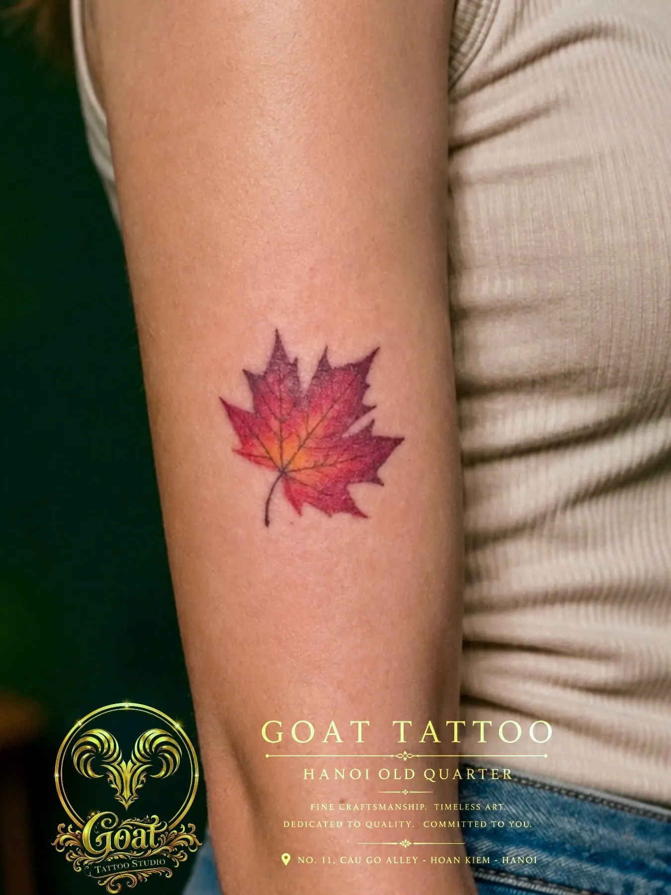 Watercolor-style autumn maple leaf tattoo in red and orange tones on the forearm, by GOAT Tattoo Studio in Hanoi.