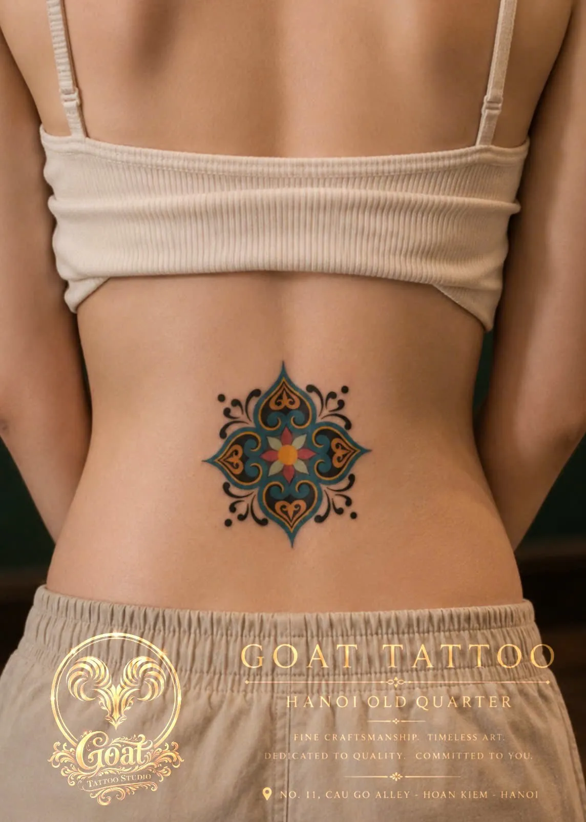 A colorful ornamental medallion tattoo in teal, gold, and red on the lower back, by GOAT Tattoo Studio Hanoi.