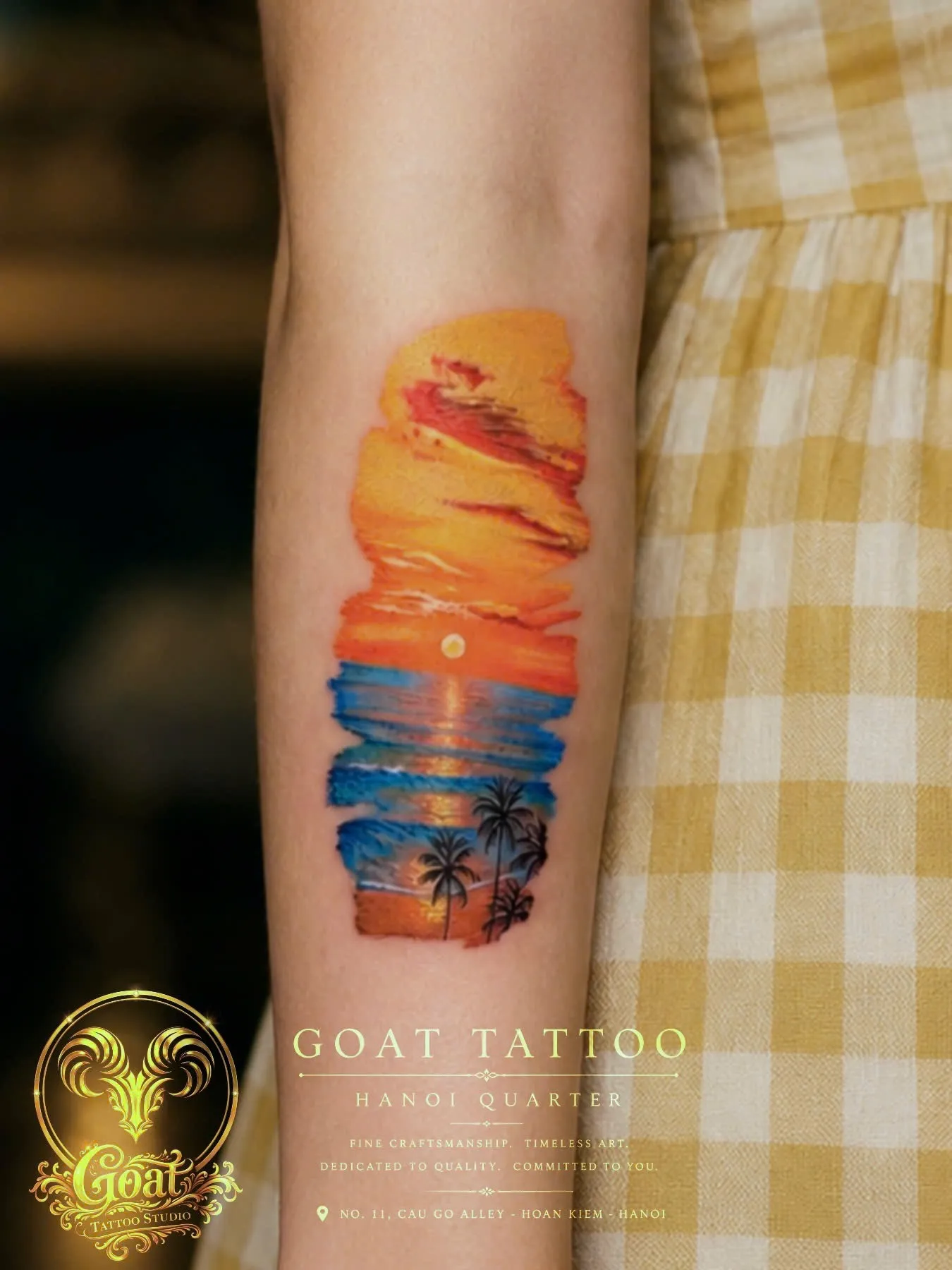 Watercolor-style sunset seascape with palm trees tattooed vertically on the forearm, by GOAT Tattoo Studio in Hanoi.