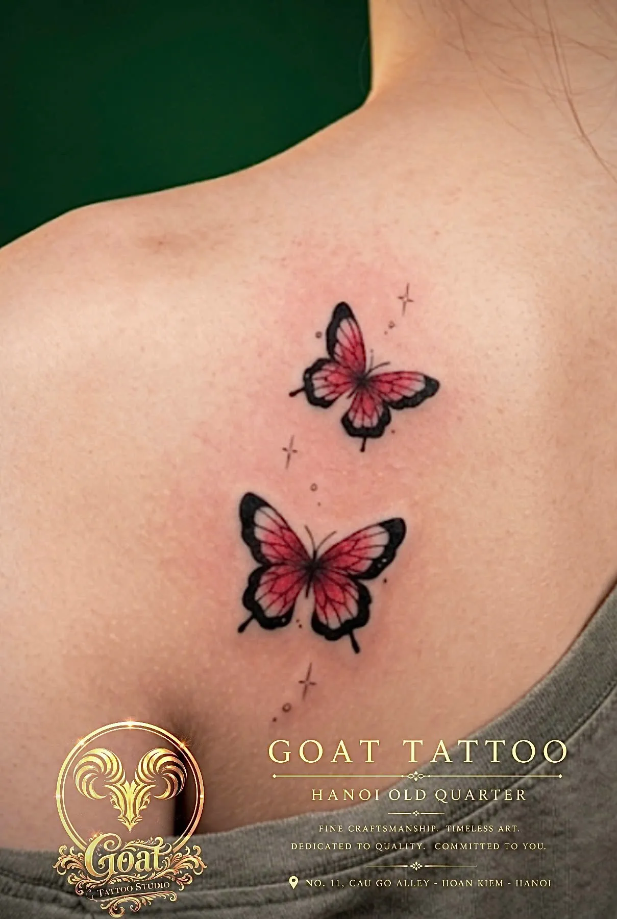 Colorful illustrative tattoo of two pink and black butterflies fluttering across the shoulder blade, by GOAT Tattoo Studio in Hanoi.