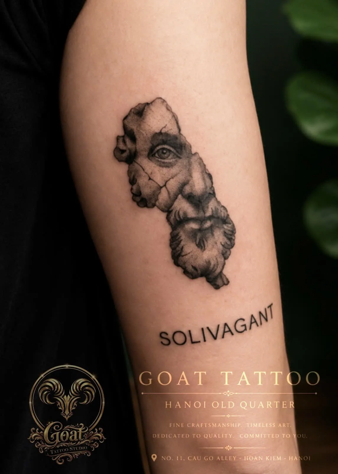 A fine-line black and grey forearm tattoo of a fractured stone bust with the word "Solivagant" inked beneath it, done at GOAT Tattoo Studio in Hanoi's Old Quarter.