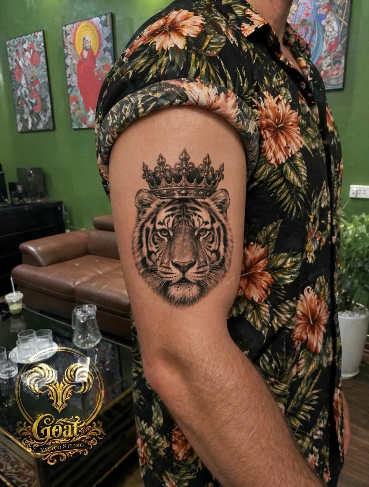 Realistic tiger portrait wearing a royal crown tattooed on the upper arm, by GOAT Tattoo Studio in Hanoi.