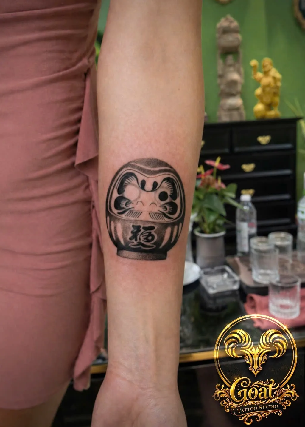 Black and grey Japanese daruma doll tattoo on the forearm, by GOAT Tattoo Studio in Hanoi's Old Quarter.