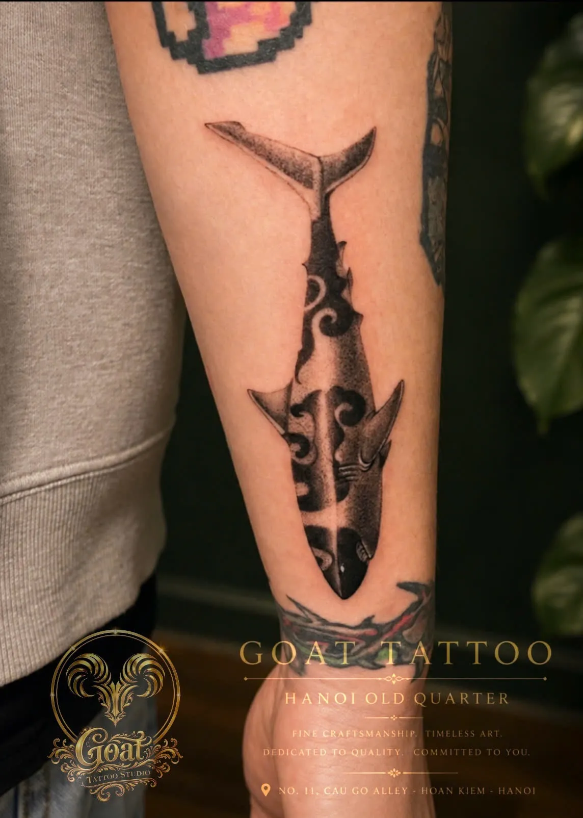 A bold black dotwork shark tattoo detailed with tribal Maori-inspired patterns running down the forearm, done at GOAT Tattoo Studio in Hanoi's Old Quarter.