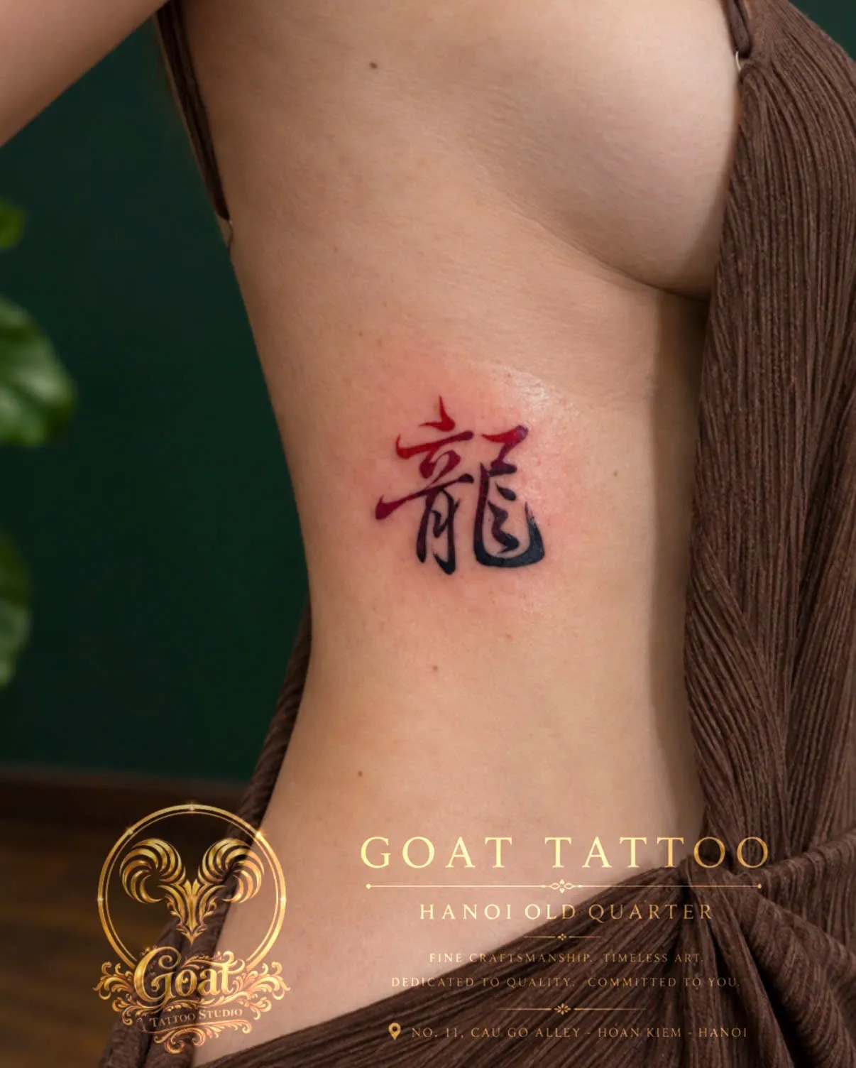 The Chinese character for dragon in a red-to-black gradient, tattooed on the ribs, by GOAT Tattoo Studio Hanoi.
