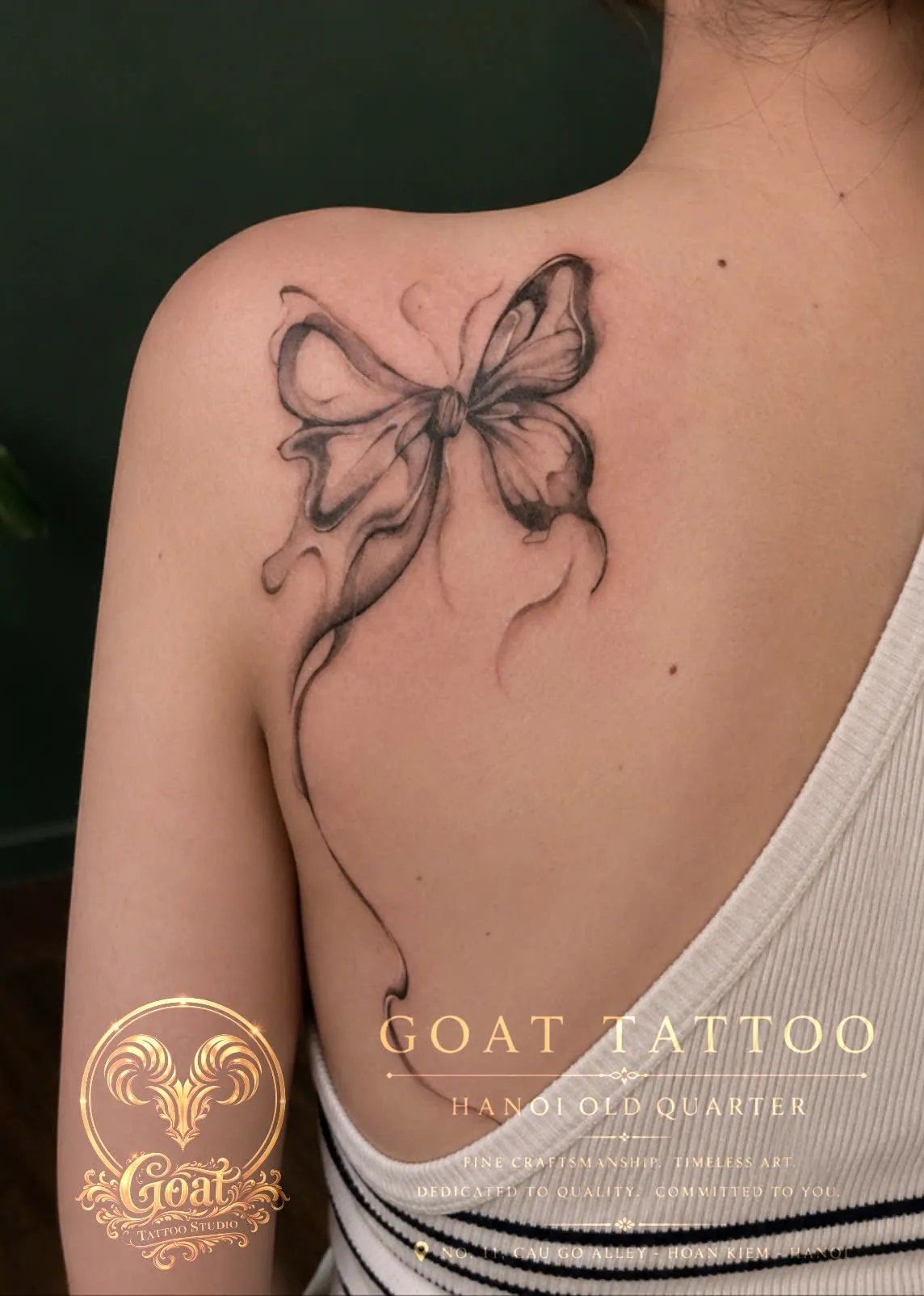 Fine line butterfly-shaped ribbon tattoo flowing across the shoulder blade, by GOAT Tattoo Studio in Hanoi.
