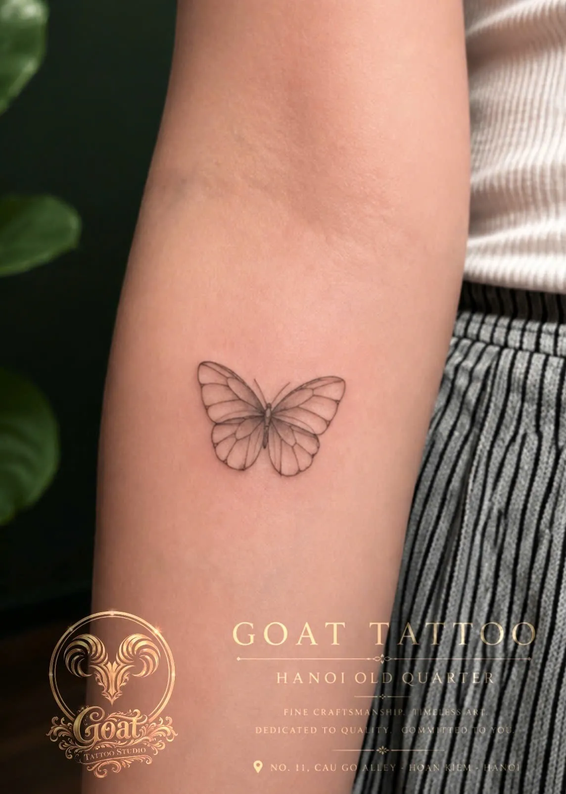 A delicate fine-line black tattoo of a butterfly with detailed wing patterns on the forearm, done at GOAT Tattoo Studio in Hanoi's Old Quarter.