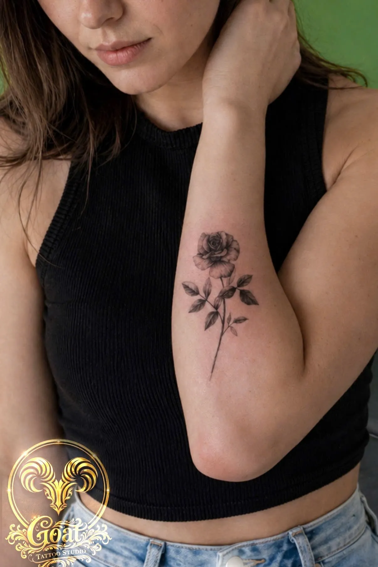 Fine line black rose with leaves tattooed on the inner bicep, by GOAT Tattoo Studio in Hanoi.