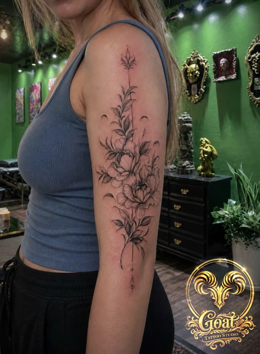 Fine line floral vine and arrow tattoo running along the upper arm, by GOAT Tattoo Studio in Hanoi's Old Quarter.
