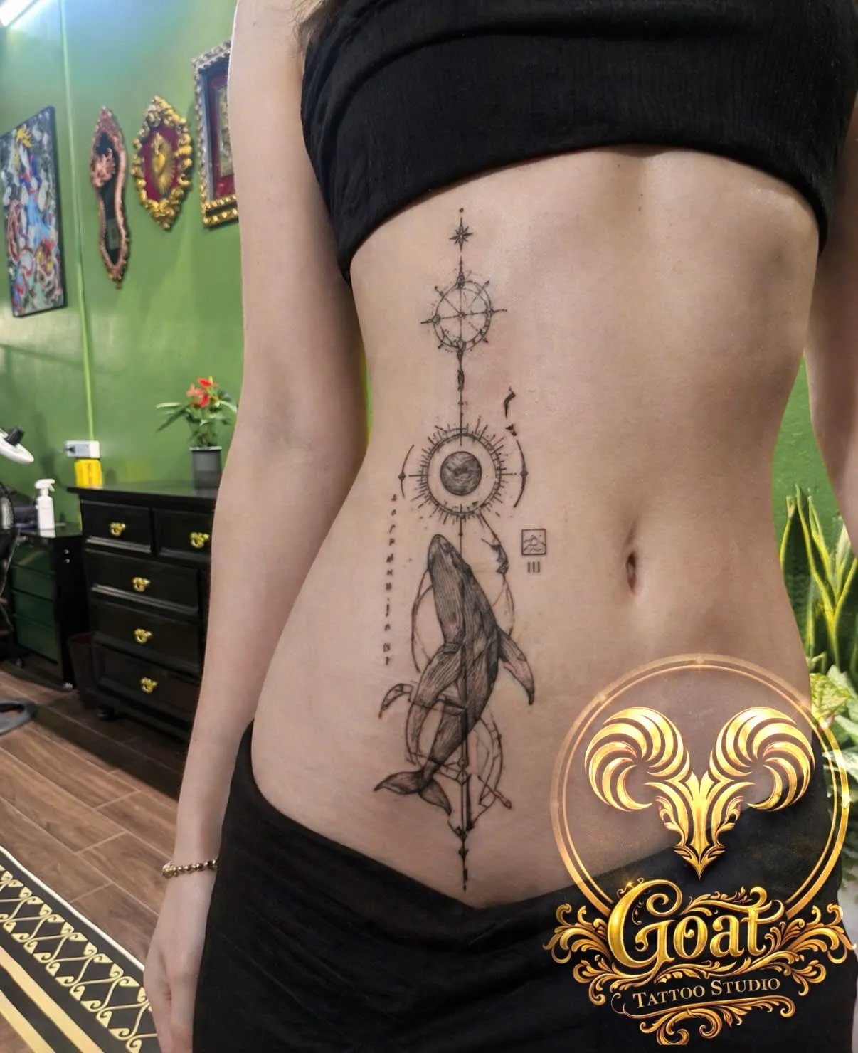 Fine line whale tattoo paired with a compass and geometric symbols along the ribs, GOAT Tattoo Studio Hanoi.