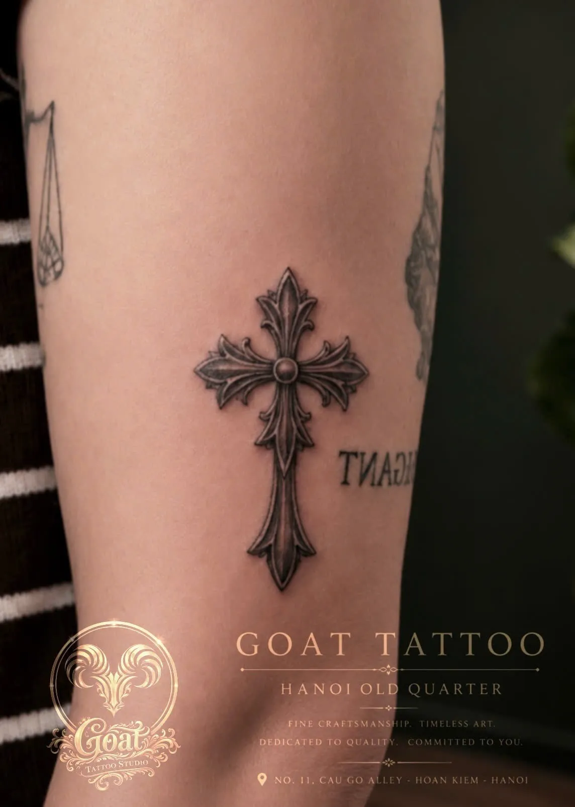 A detailed black and grey ornate gothic cross tattoo with dimensional filigree shading on the forearm, done at GOAT Tattoo Studio in Hanoi's Old Quarter.