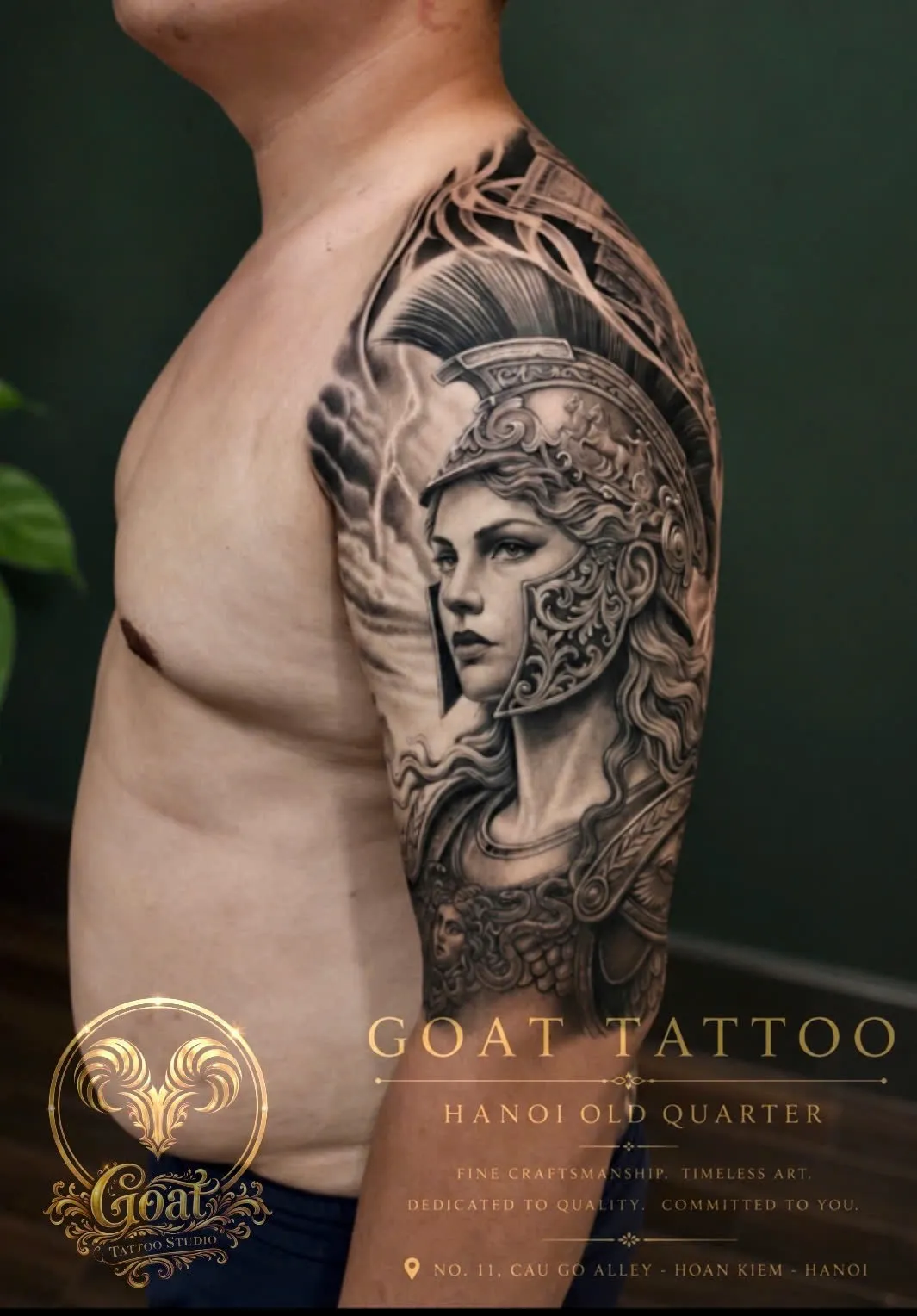 Black and grey realism tattoo of a helmeted warrior goddess portrait on the upper arm, by GOAT Tattoo Studio in Hanoi.
