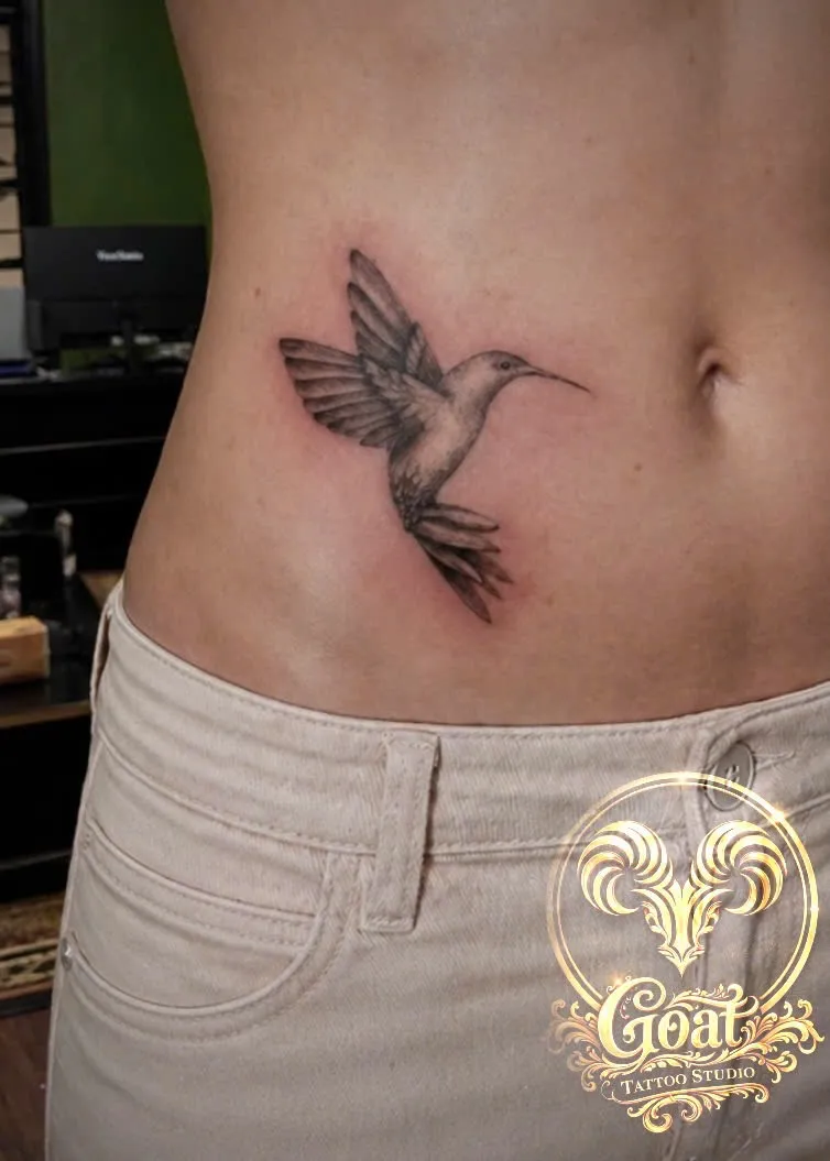Detailed black and grey hummingbird tattoo on the side torso, by GOAT Tattoo Studio in Hanoi.