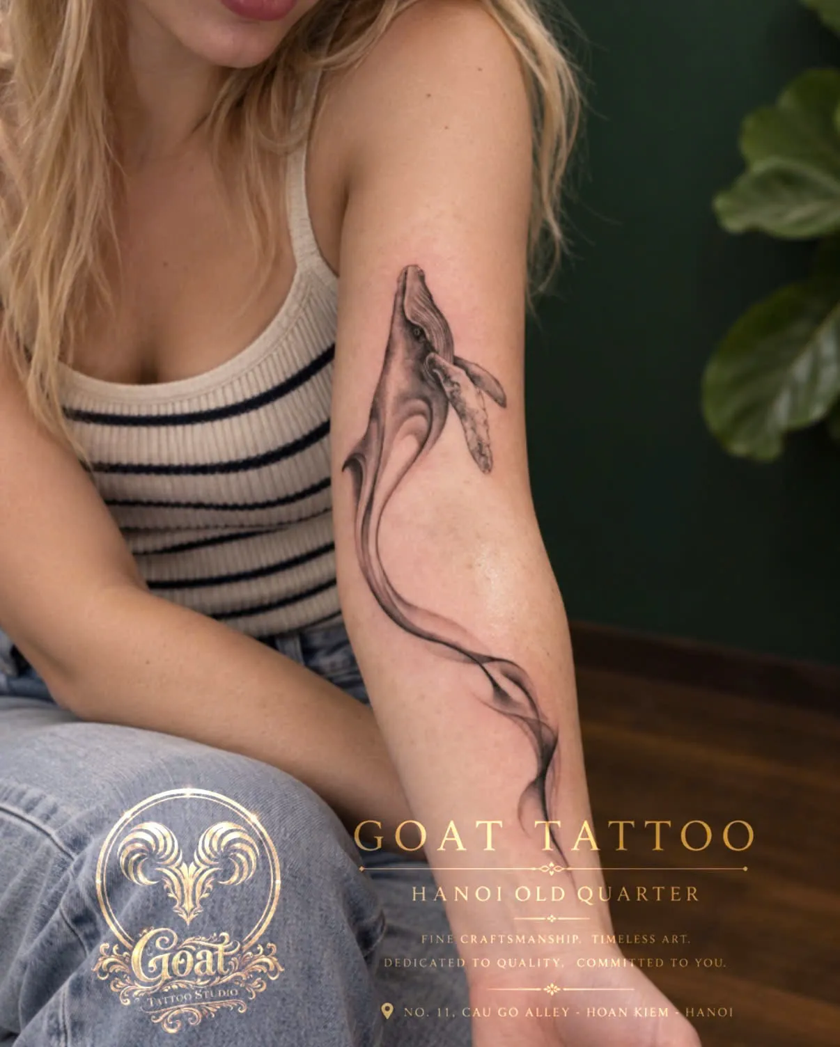 A black and grey realism humpback whale tattoo diving down the arm, by GOAT Tattoo Studio in Hanoi's Old Quarter.