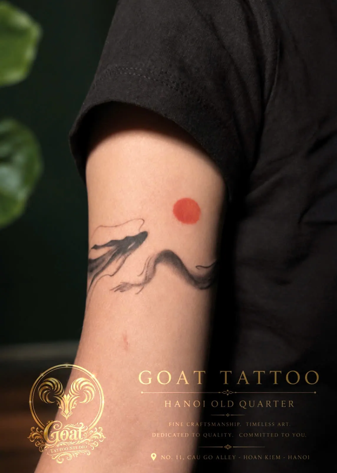 An expressive ink-wash style dragon silhouette curling beneath a bold red sun on the upper arm, done at GOAT Tattoo Studio in Hanoi's Old Quarter.