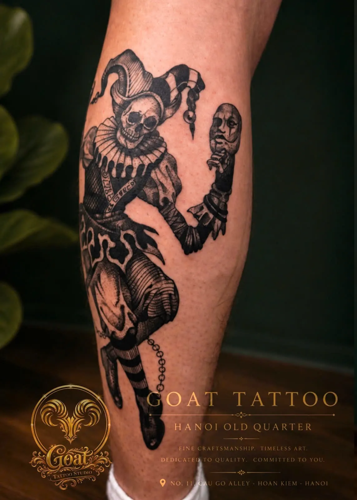 A bold blackwork tattoo of a skeletal jester in a ruffled collar holding a theatrical mask on the calf, done at GOAT Tattoo Studio in Hanoi's Old Quarter.
