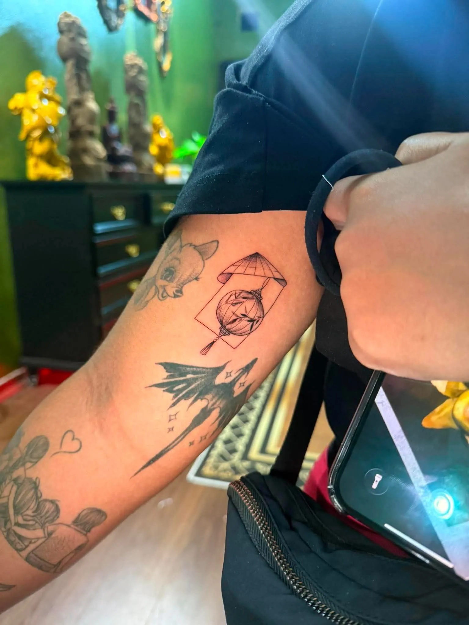 A fine-line forearm tattoo combining a Vietnamese lantern postage-stamp design with a dragon silhouette trailing stars, done at GOAT Tattoo Studio in Hanoi's Old Quarter.