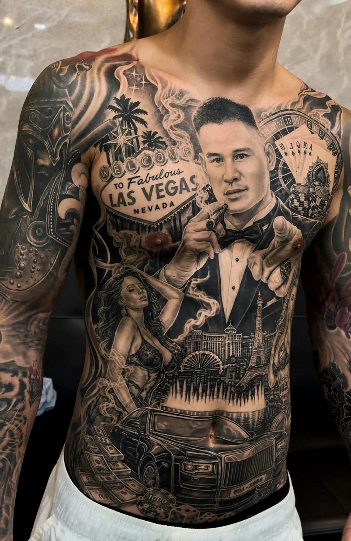 Black and grey realism tattoo telling a Las Vegas casino story across the full torso, by GOAT Tattoo Studio in Hanoi.