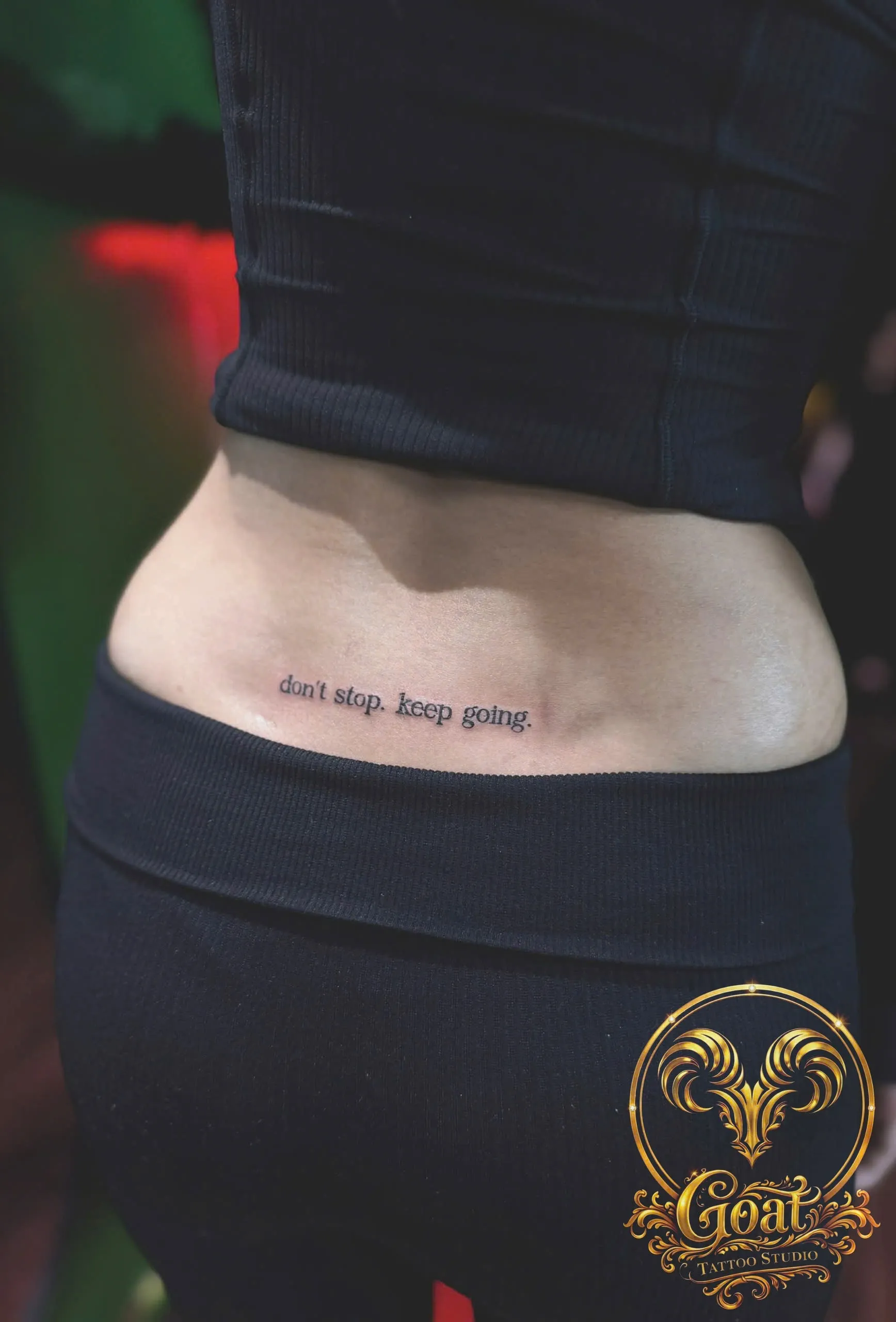 Small serif script tattoo reading 'don't stop, keep going' on the lower back, by GOAT Tattoo Studio Hanoi.