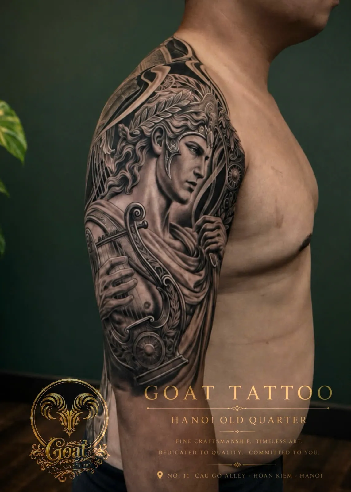 Black and grey realism tattoo of a classical figure wearing a laurel wreath and holding a lyre, on the shoulder, by GOAT Tattoo Studio Hanoi.