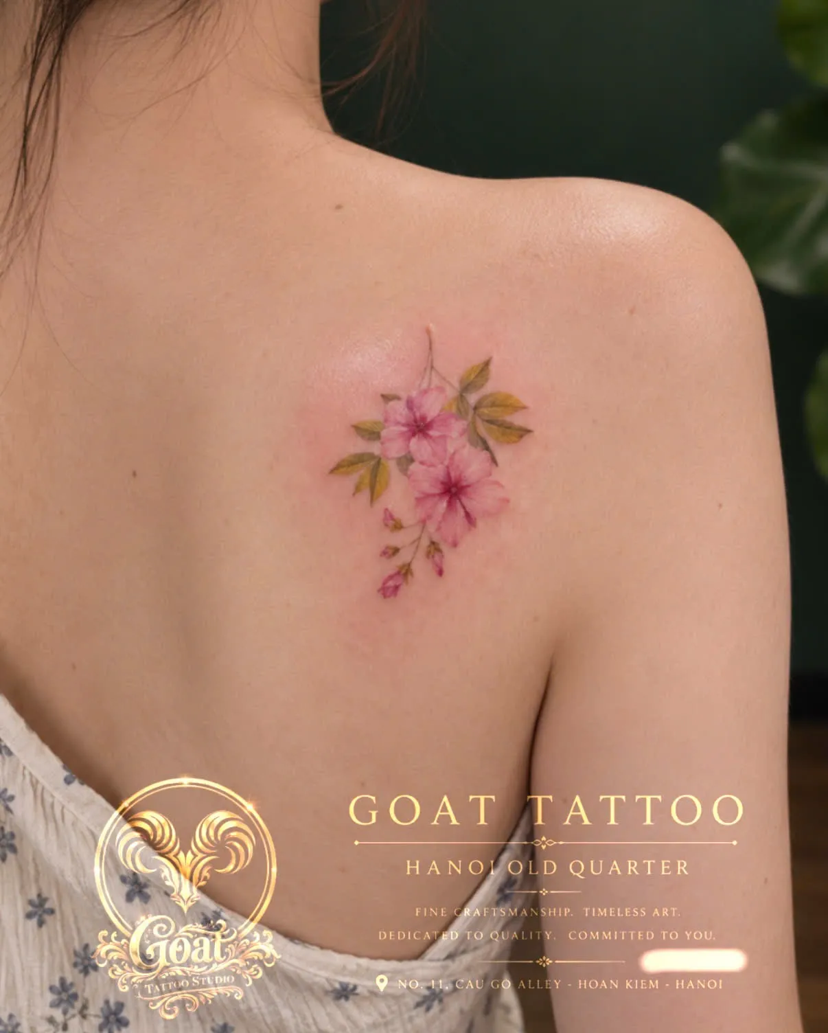 A cluster of soft pink watercolor-style flowers tattooed on the shoulder blade, by GOAT Tattoo Studio in Hanoi's Old Quarter.