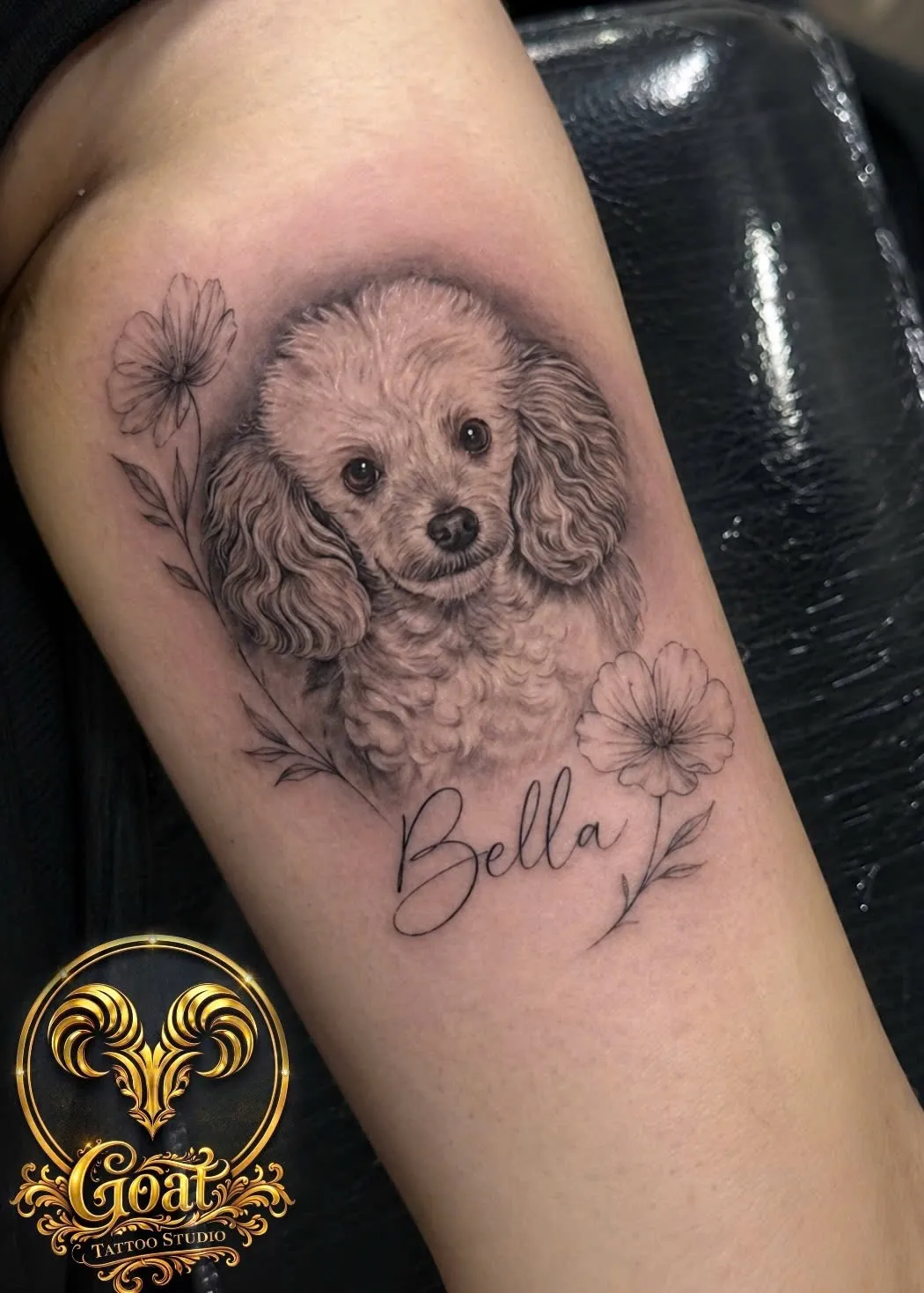 Black and grey poodle portrait named 'Bella' with fine line flowers on the forearm, by GOAT Tattoo Studio Hanoi.