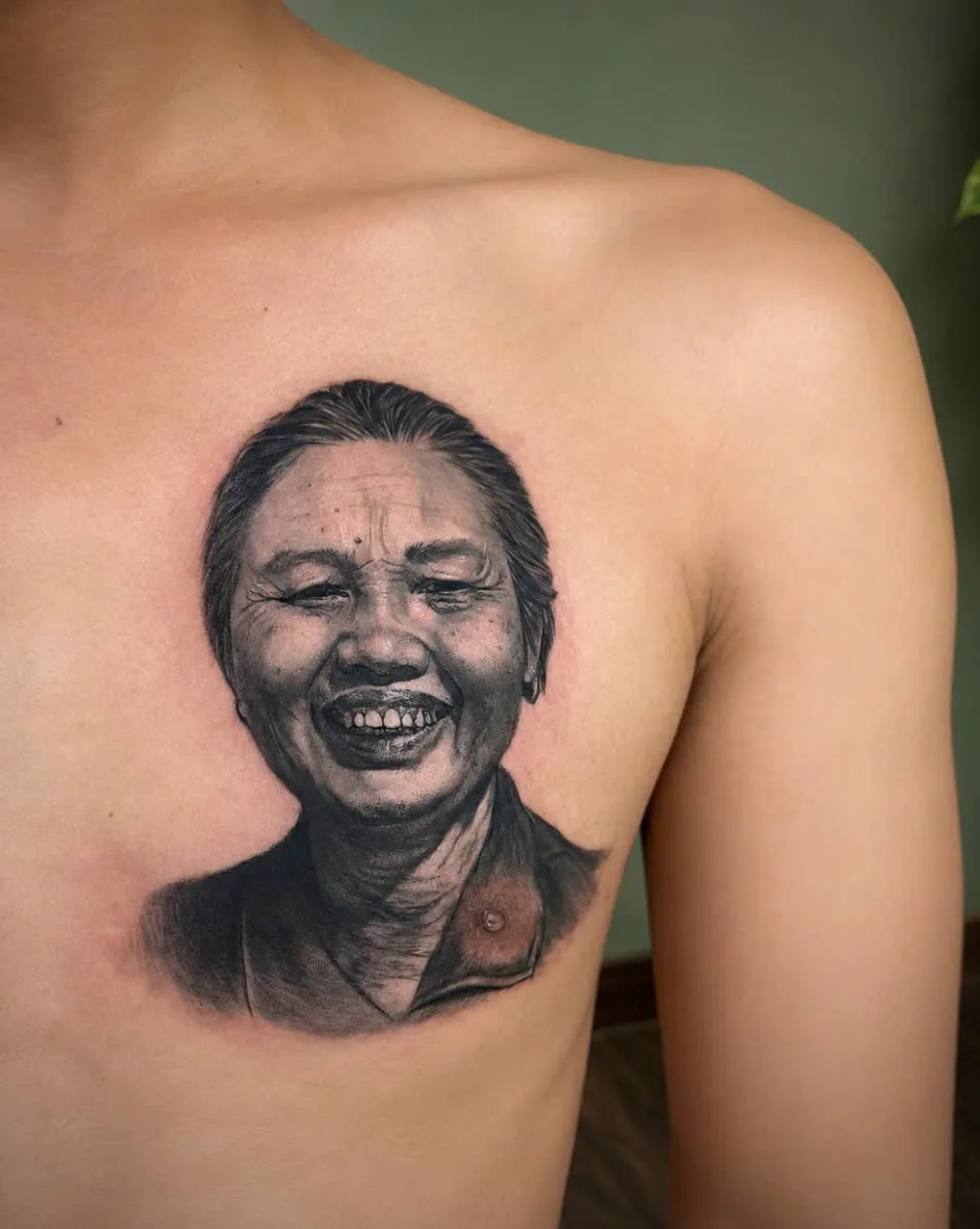 Black and grey realism portrait tattoo of an elderly woman on the chest, by GOAT Tattoo Studio in Hanoi.