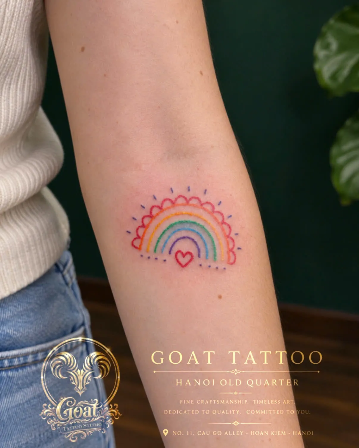 A colorful fine line rainbow tattoo with a small heart underneath, on the forearm, by GOAT Tattoo Studio in Hanoi's Old Quarter.