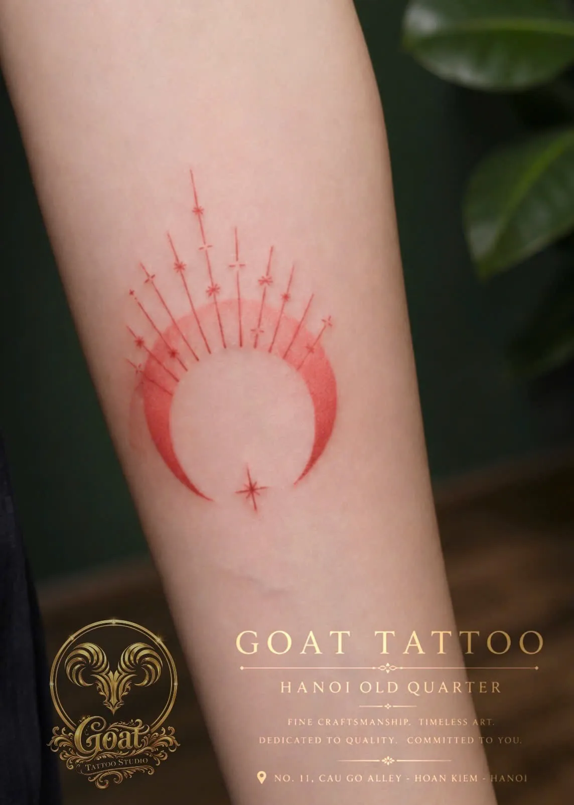 A soft red fine-line tattoo of a crescent moon crowned with radiating sunburst rays on the forearm, done at GOAT Tattoo Studio in Hanoi's Old Quarter.