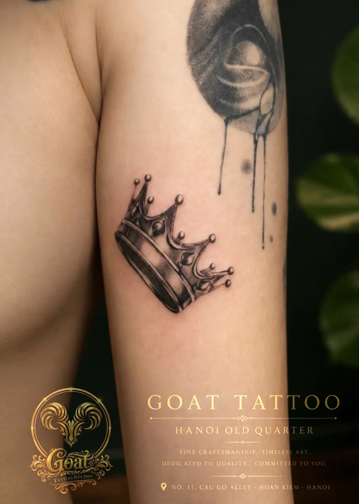 A detailed black and grey dotwork tattoo of a jeweled royal crown on the upper arm, done at GOAT Tattoo Studio in Hanoi's Old Quarter.