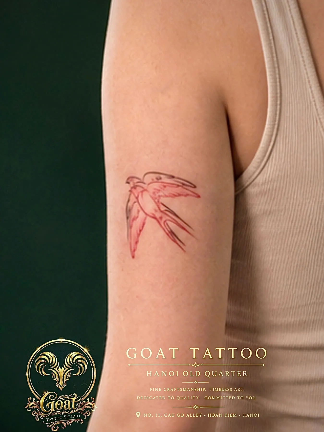Sketch-style swallow tattoo rendered in red and black linework on the upper arm, by GOAT Tattoo Studio in Hanoi.