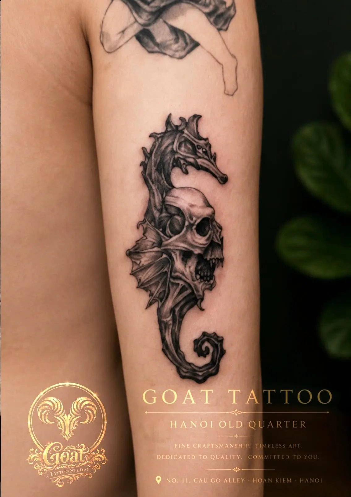 A dark black and grey tattoo of a seahorse fused with a bat-winged skull along the forearm, done at GOAT Tattoo Studio in Hanoi's Old Quarter.