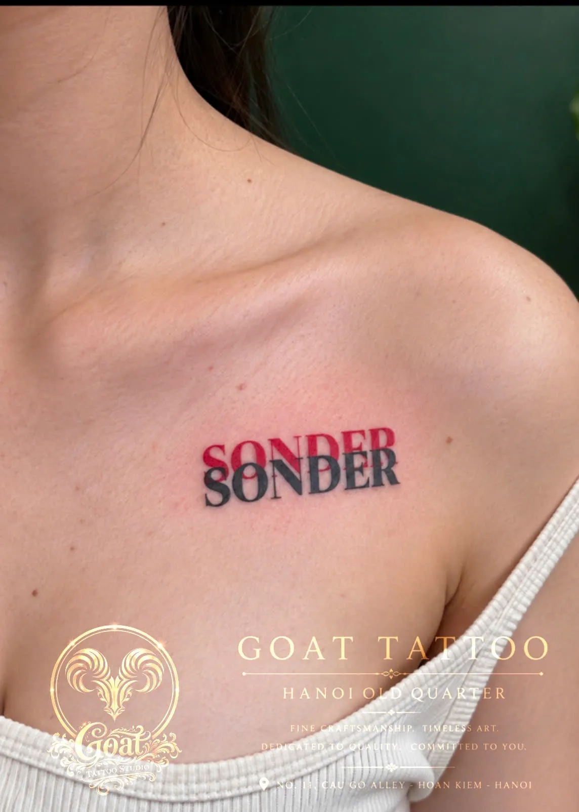 The word Sonder repeated in overlapping red and black typography, tattooed on the collarbone, by GOAT Tattoo Studio in Hanoi's Old Quarter.
