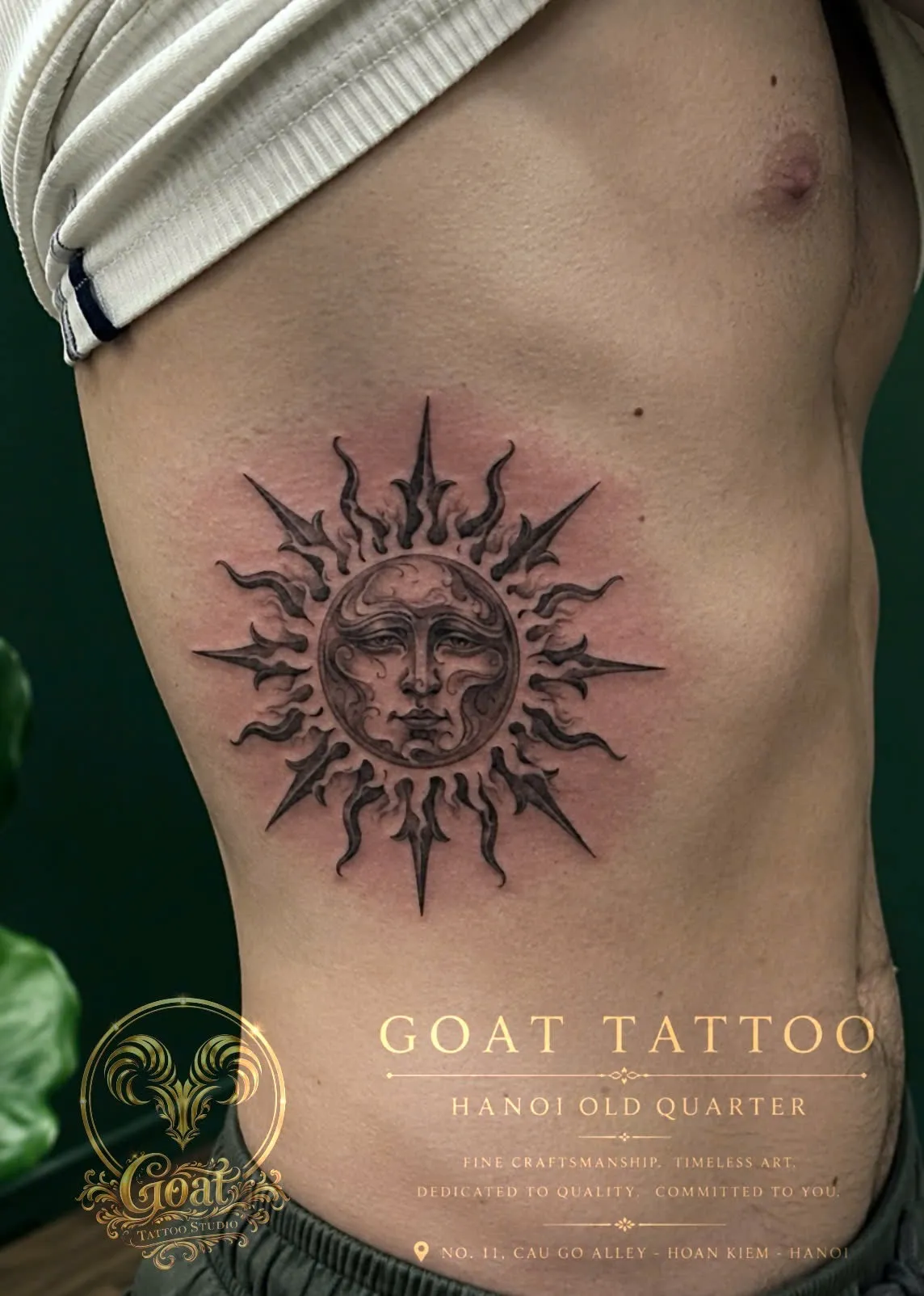 A black and grey realism sun tattoo with a detailed face at its center, on the ribs, by GOAT Tattoo Studio in Hanoi's Old Quarter.