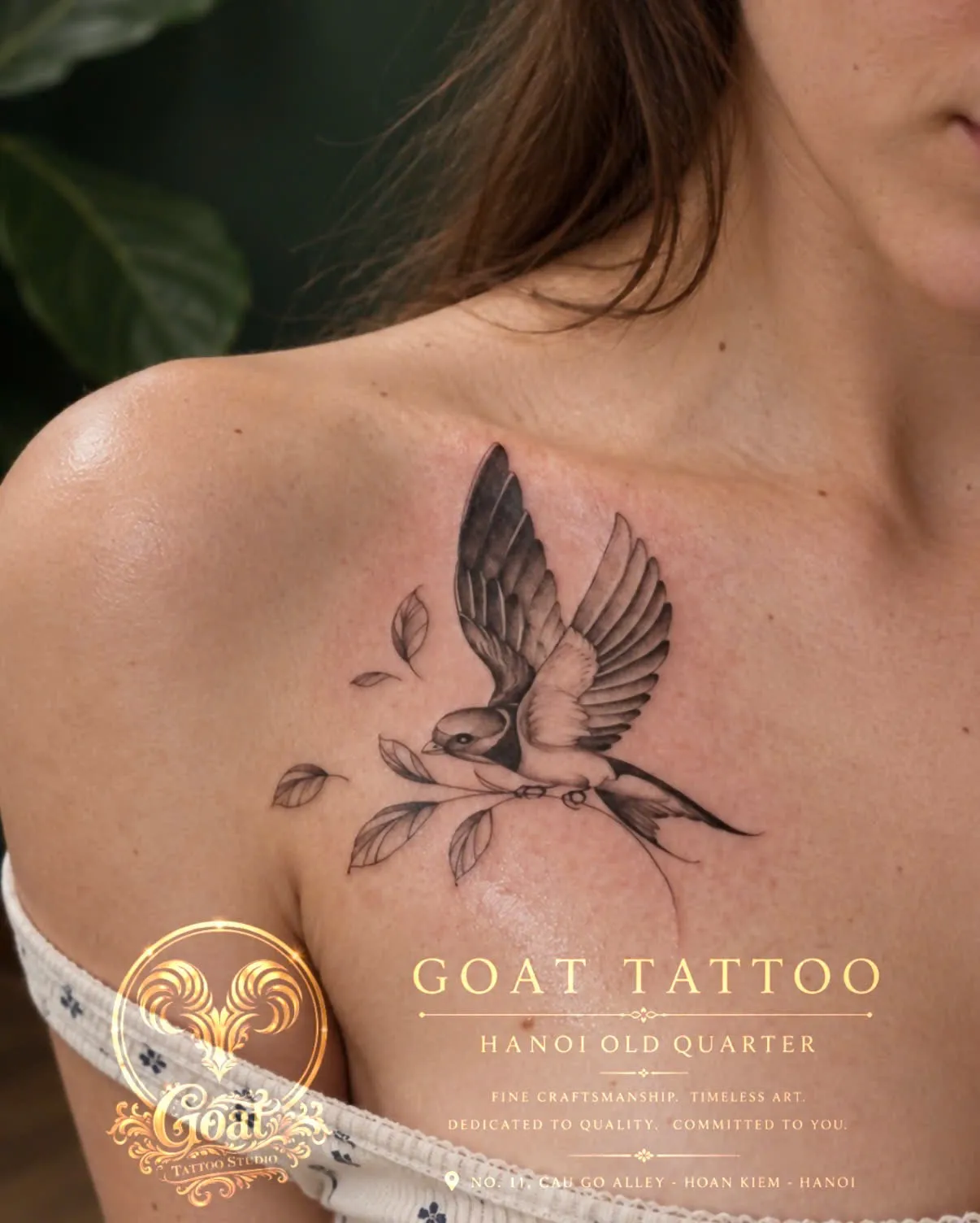 A black and grey realism swallow perched on a branch, tattooed across the collarbone, by GOAT Tattoo Studio Hanoi.