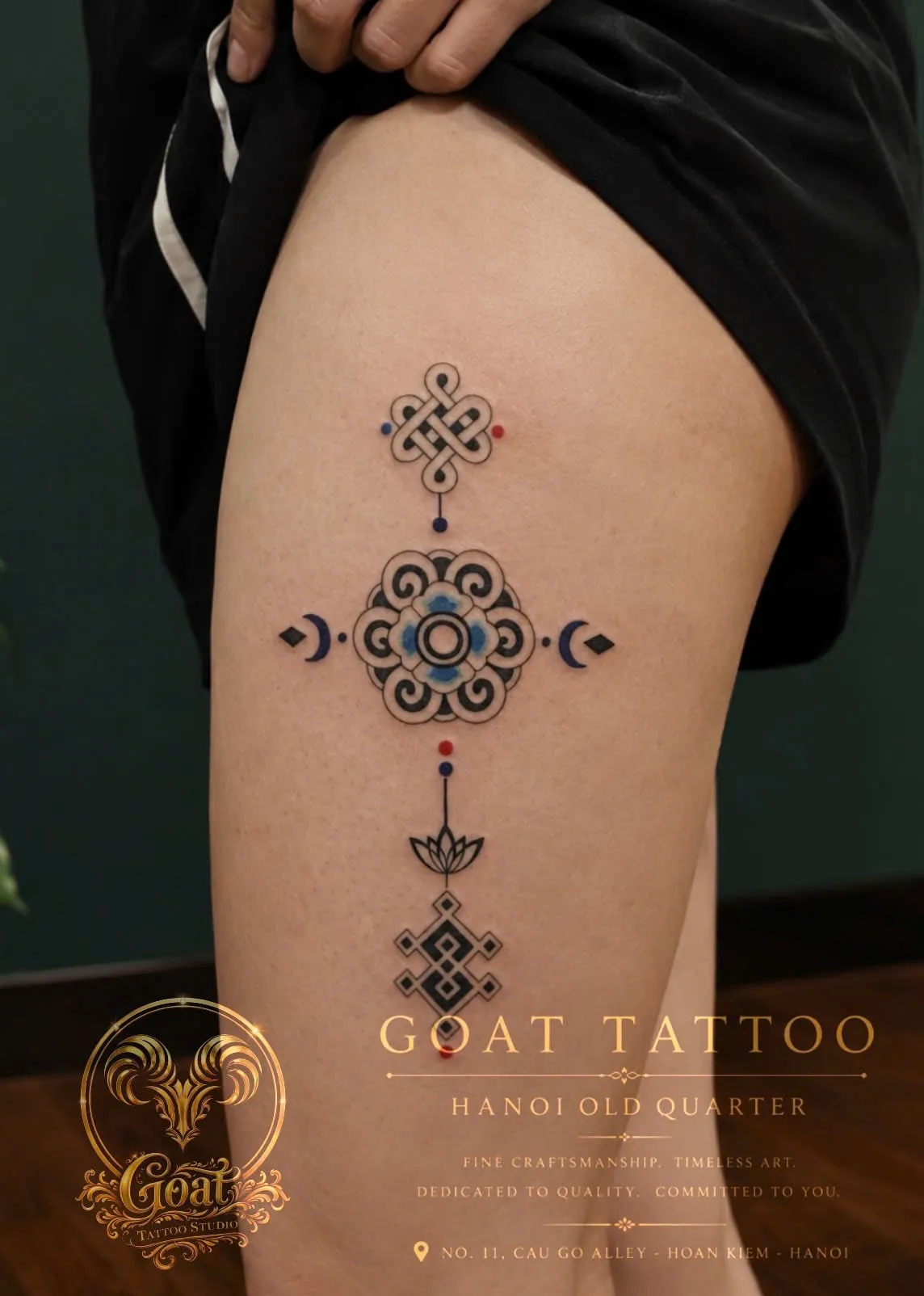 A vertical row of Tibetan-inspired symbols including an endless knot and lotus, tattooed on the thigh, by GOAT Tattoo Studio in Hanoi's Old Quarter.