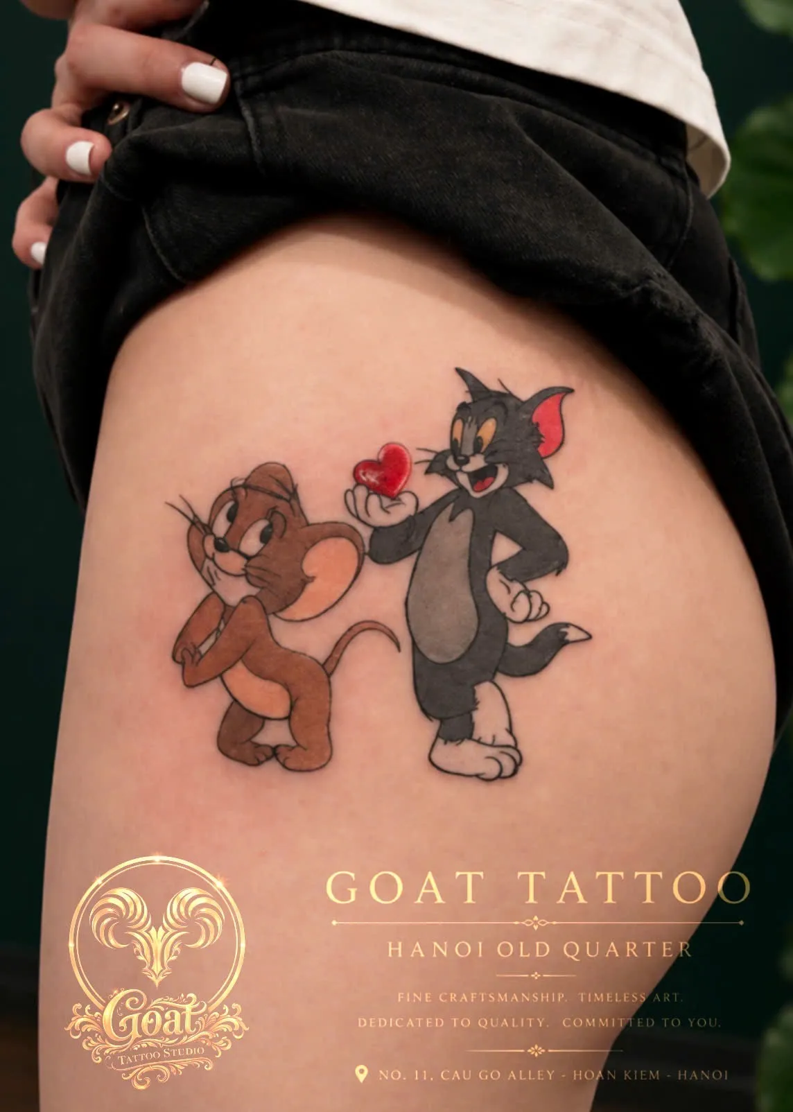 A full-color tattoo of Tom and Jerry sharing a heart, on the thigh, by GOAT Tattoo Studio in Hanoi's Old Quarter.