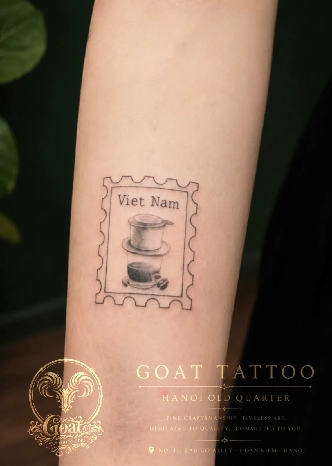 A fine-line black forearm tattoo styled as a vintage postage stamp featuring a Vietnamese phin coffee filter and the words "Viet Nam," done at GOAT Tattoo Studio in Hanoi's Old Quarter.