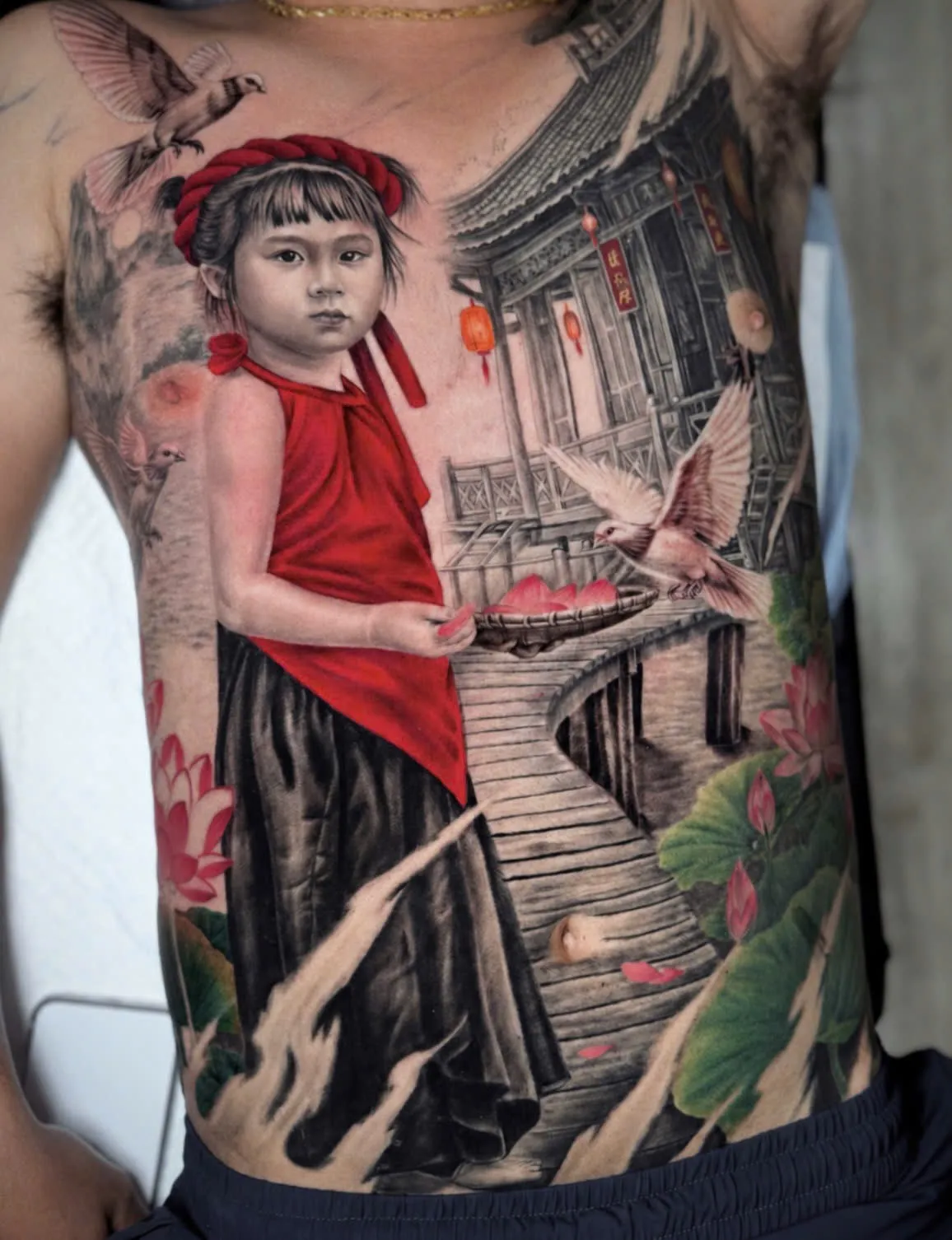 Black and grey realistic tattoo of a girl in traditional dress beside a lotus pond, covering the chest and torso, GOAT Tattoo Studio Hanoi.