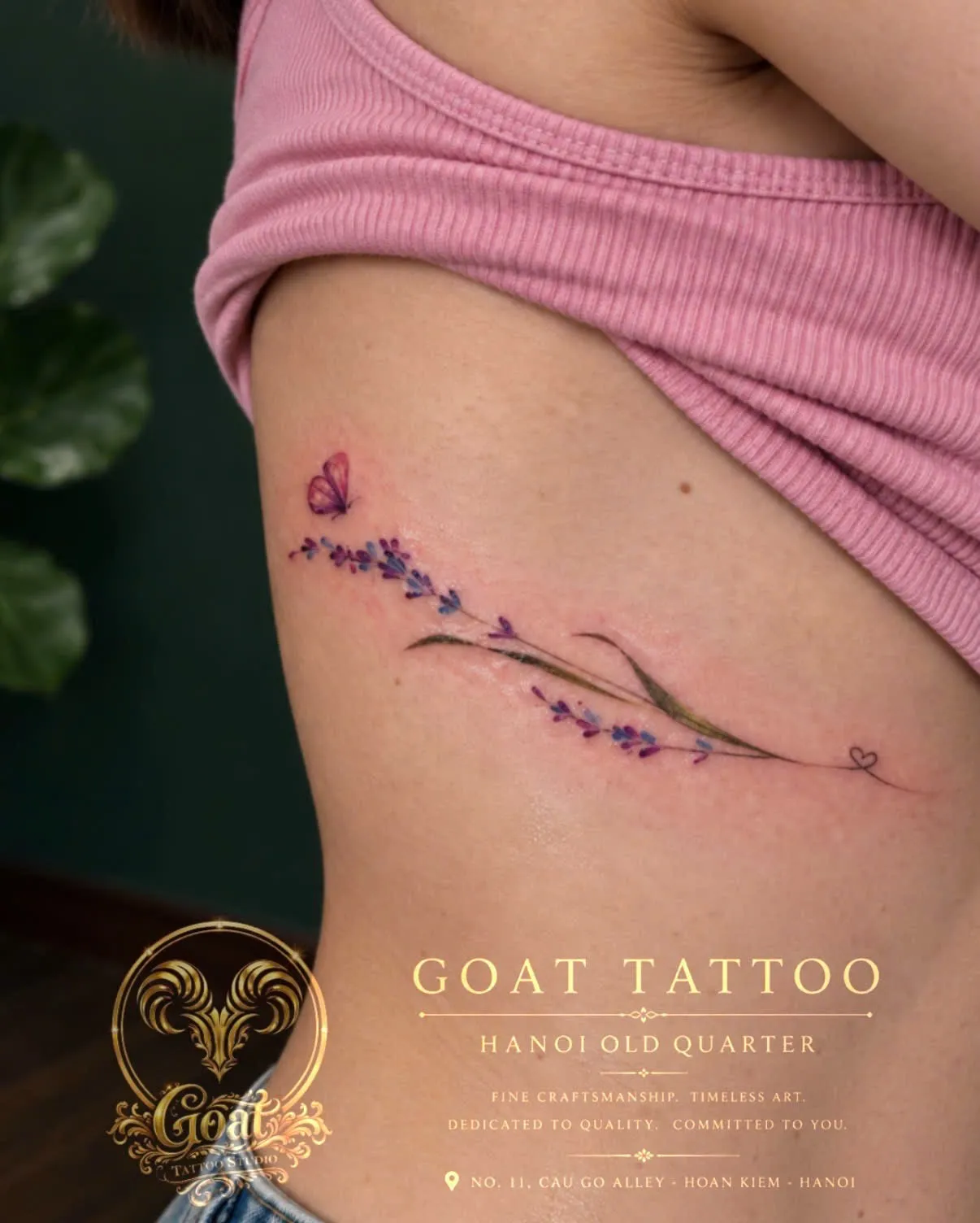 A watercolor-style lavender sprig with a small butterfly, tattooed down the ribs, by GOAT Tattoo Studio in Hanoi's Old Quarter.